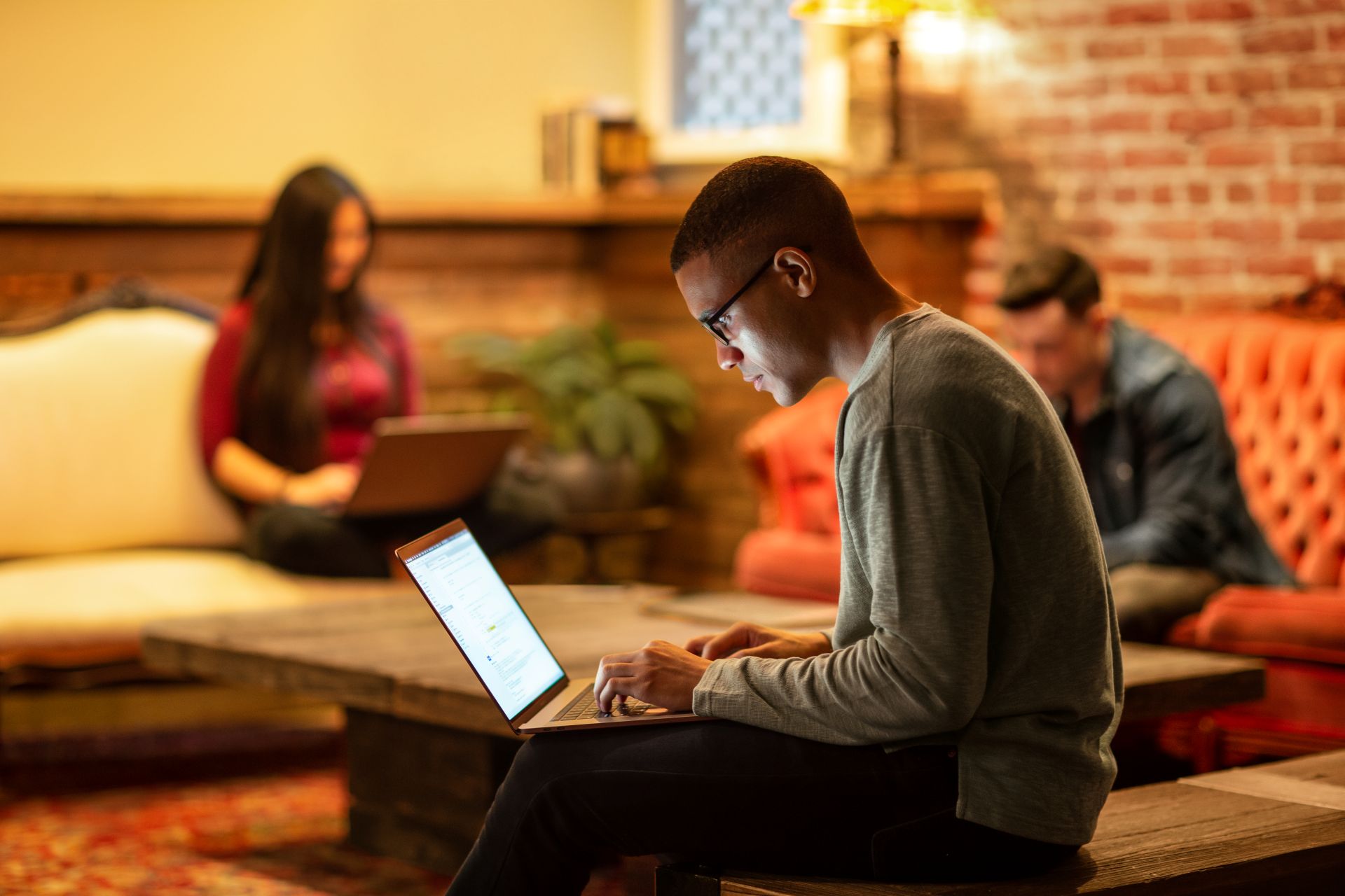 person sitting and looking at the laptop, with other people sitting and working on the laptops at the background