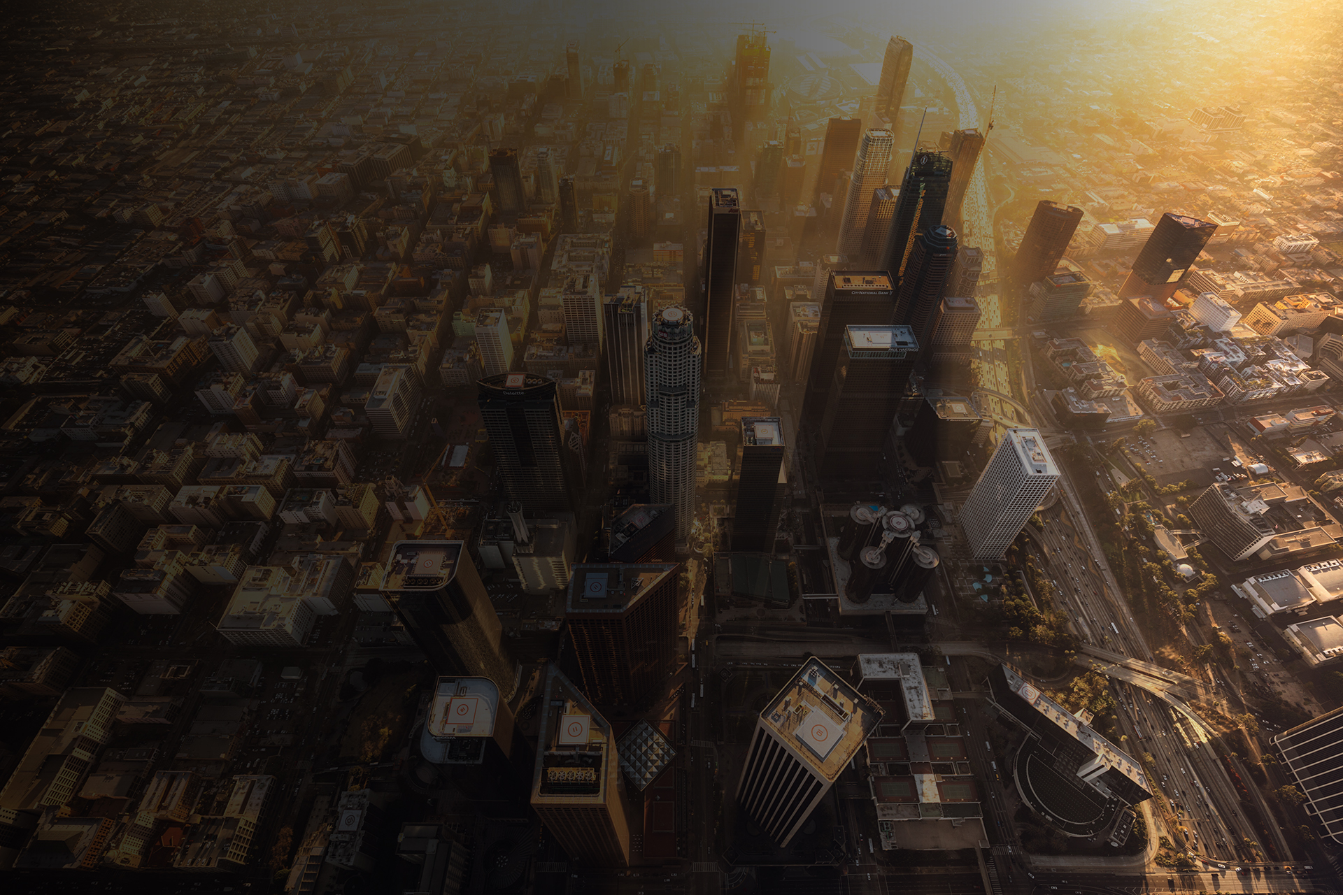 Downtown Los Angeles during a hazy sunset from a helicopter. The light rays shine gold from in between the building of DTLA.