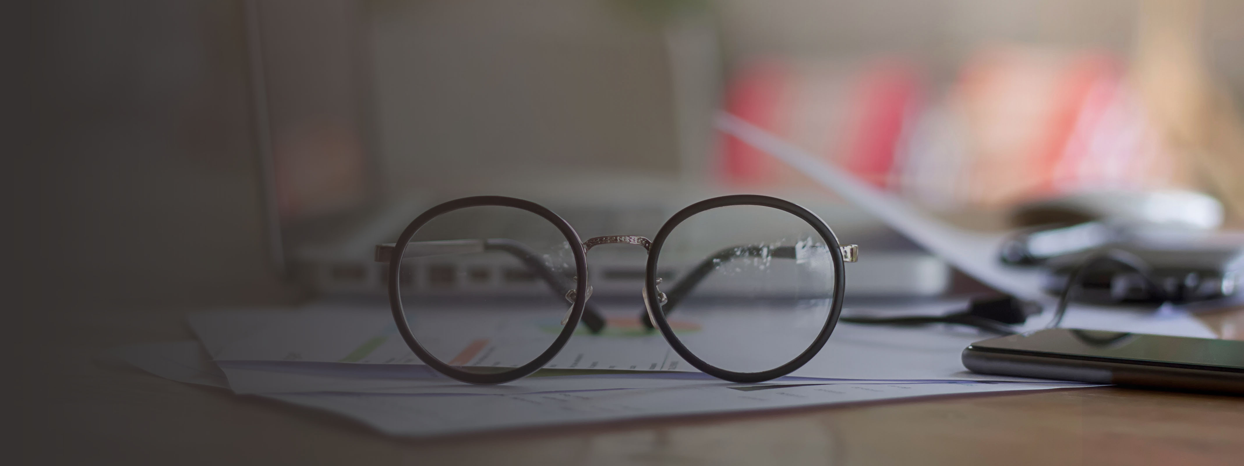 selective focus front eyeglasses on table with blur office supplies, vintage light tone.
