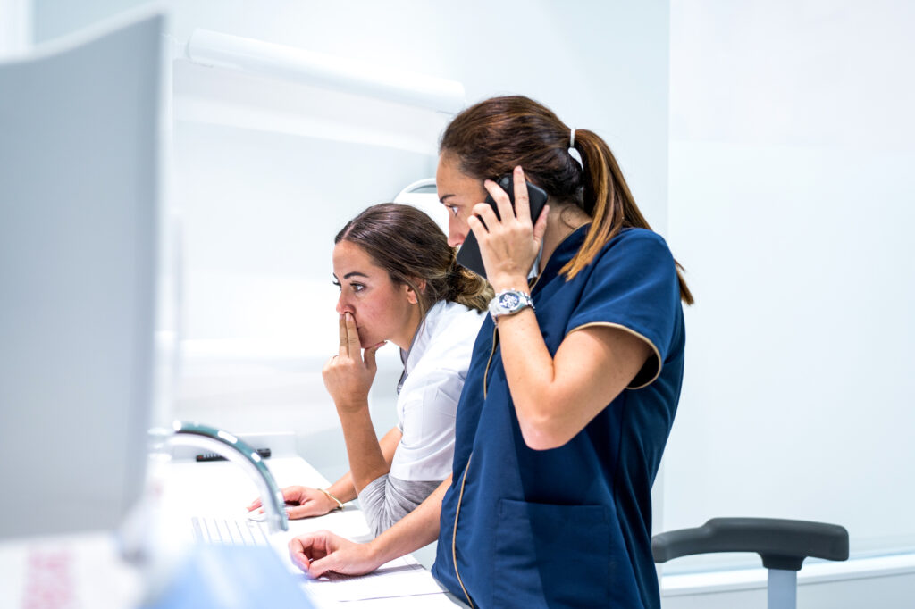 Side view of medical practitioners browsing data on modern computer while working in lab of modern hospital together and speaking on the mobile phone