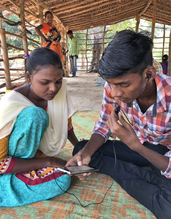 Project Karya - woman and man sitting on floor of a rural building using a cellphone