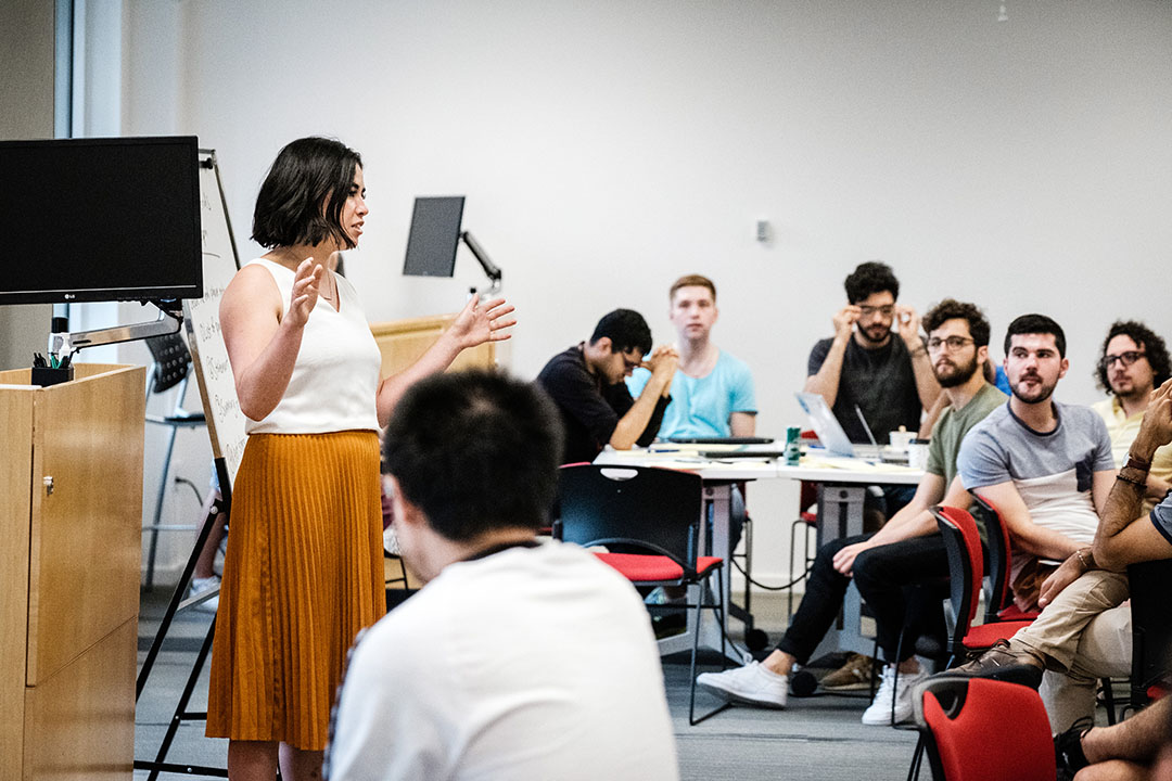 Microsoft Research Montreal female researcher presenting in front of large group of interns. Une chercheuse de Microsoft Research Montréal présente devant un grand groupe de stagiaires.