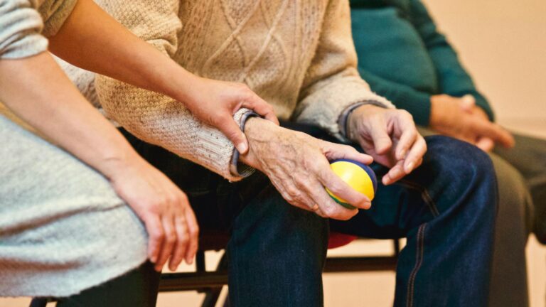 close up of a young hand holding the wrist of an older person who is holding a small ball
