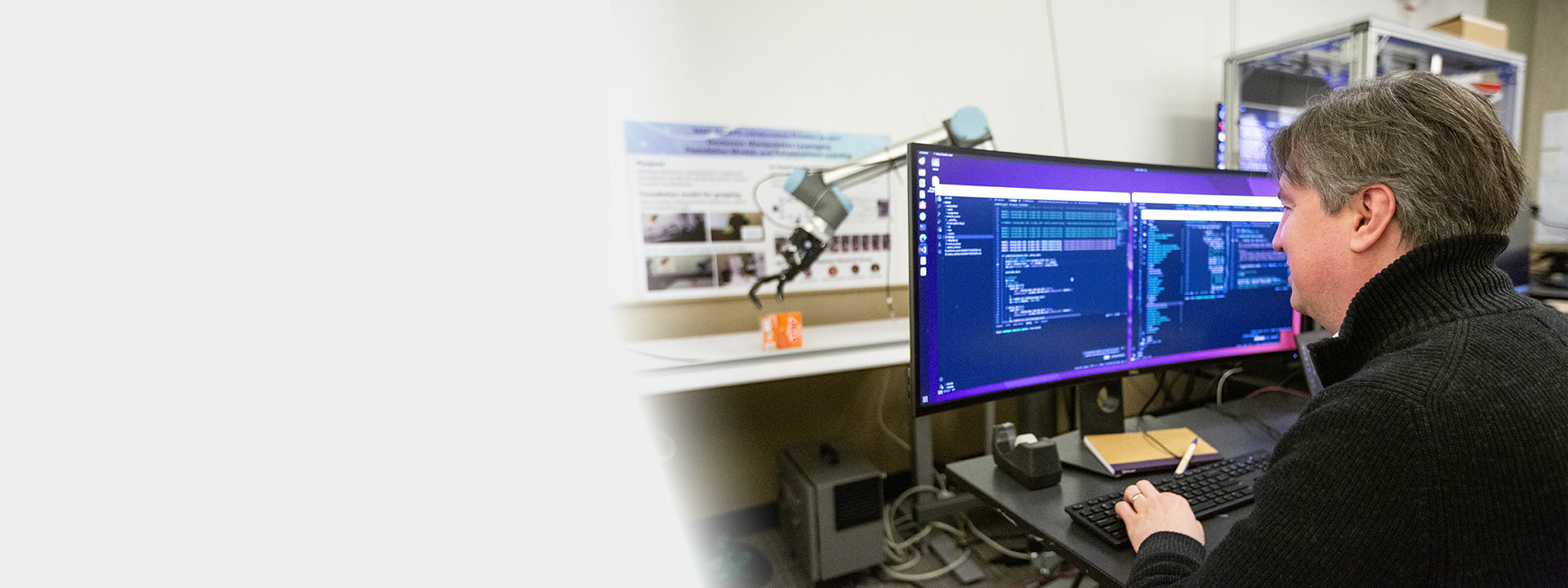 Andrey Kolobov viewing code on a large screen with a robotic hand picking up a box in the background