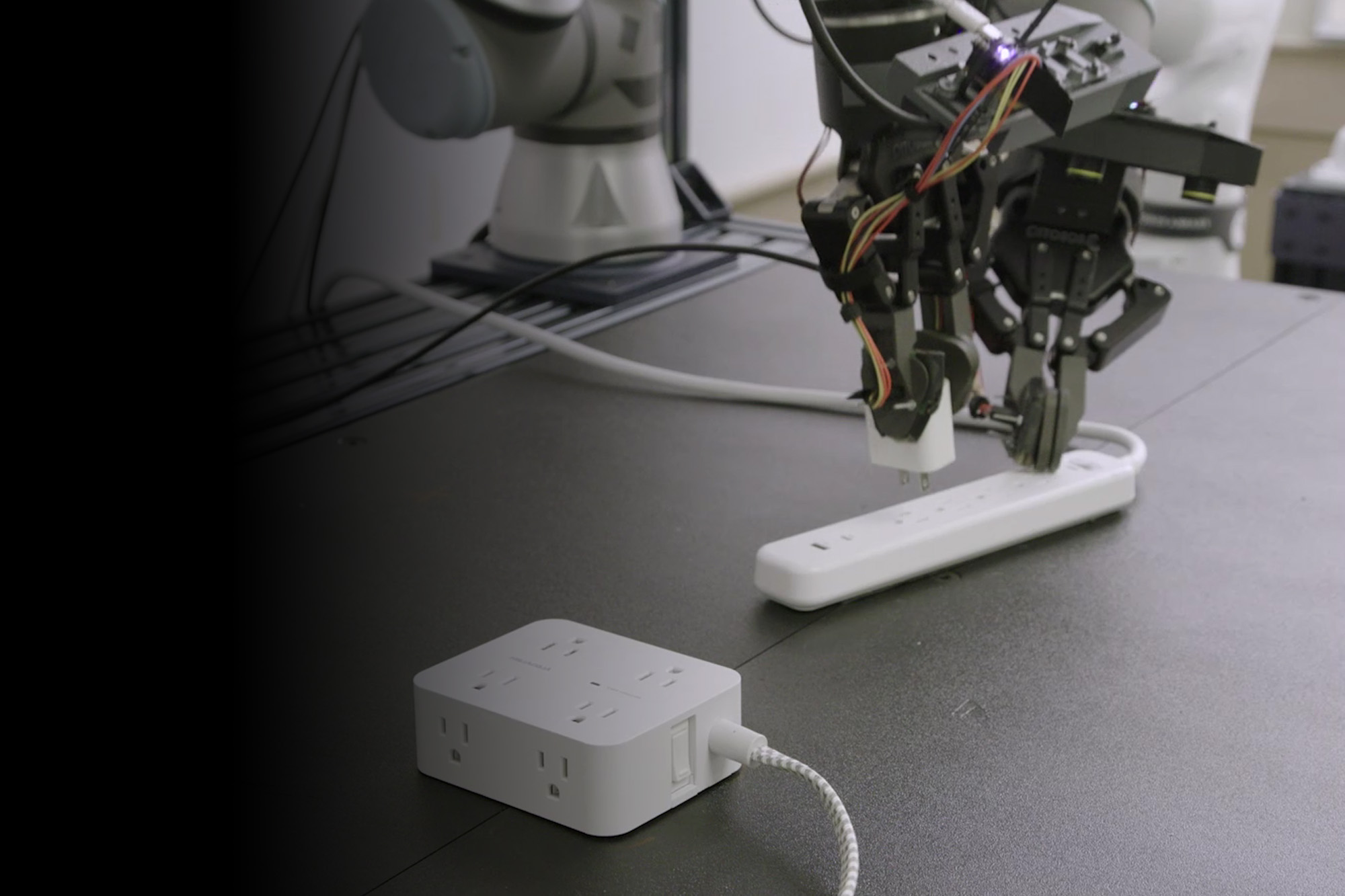 Rho-Alpha | close up image of a robotic arm and hand holding down a power outlet strip while unplugging a small charging adapter.