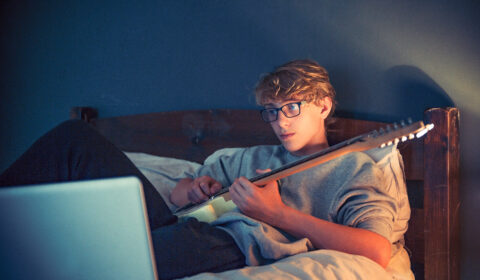 Teenager playing guitar while using AI to learn