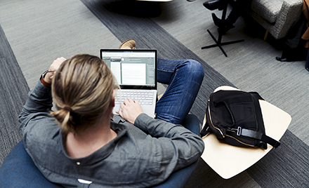 Image of a man with a pony tail seen from above working on his laptop.
