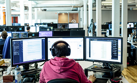 Image of a tech worker working on three monitors.