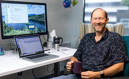 Image of a developer sitting with a cup of coffee at his desk.