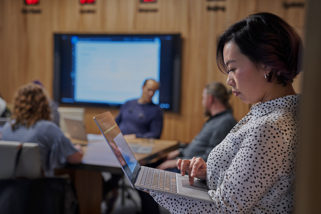 Women looking at Surface laptop with background of a conference room.