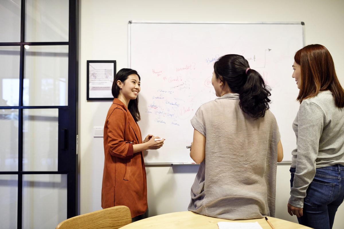Three women grouped around whiteboard brainstorming ideas.