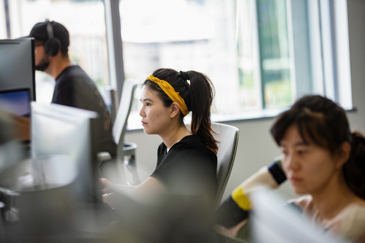 An employee in the tech industry works at a shared desk with other employees in their office.
