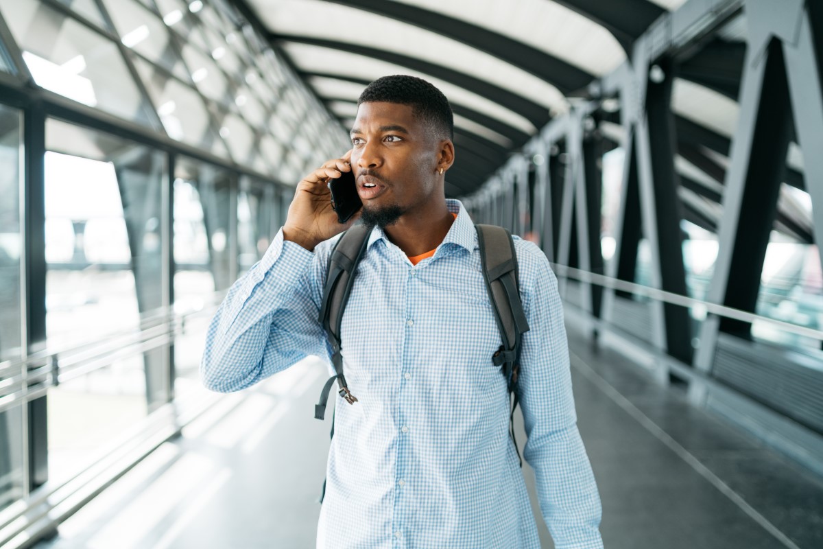 A young man walks through an airport talking on the phone.
