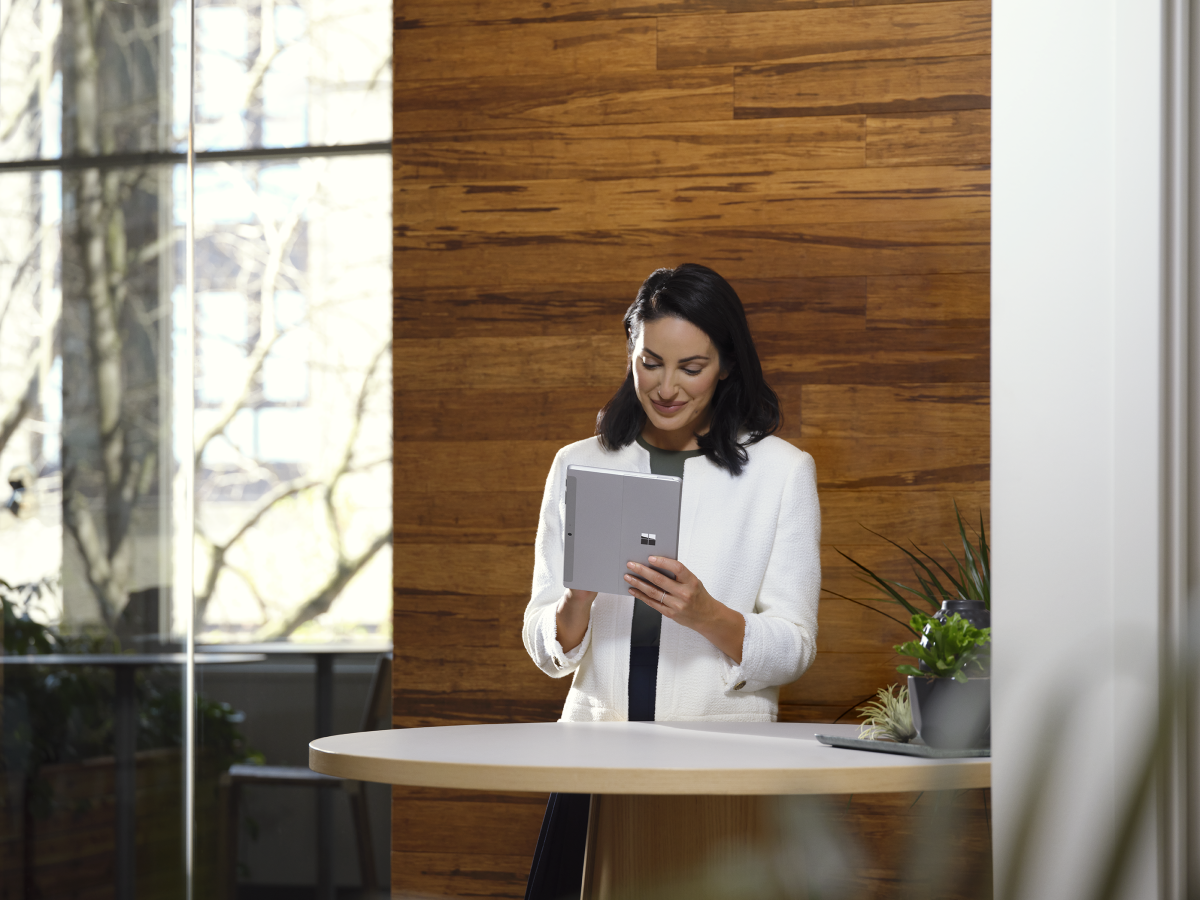 Adult female holding a platinum Surface Go 3 in tablet mode while in an office setting.