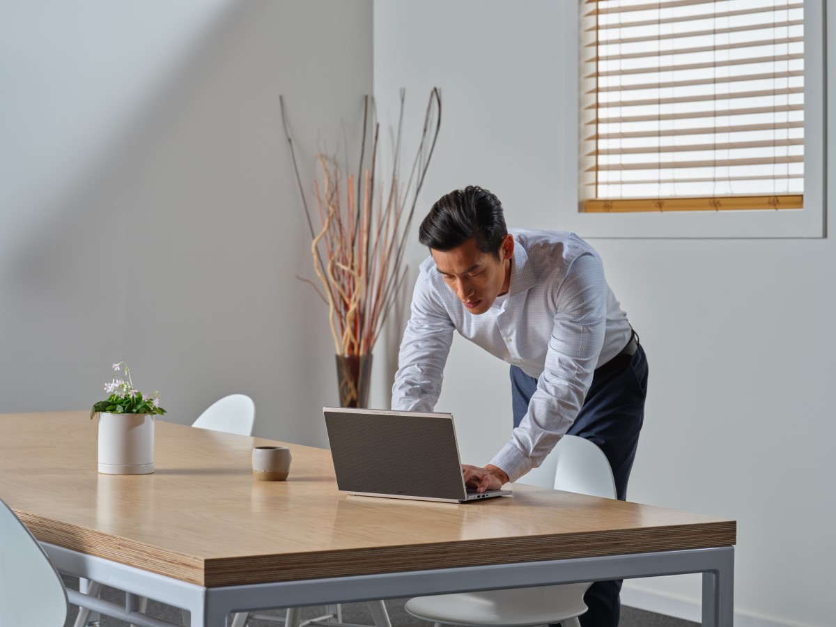 Business person leans over desk to use Acer Porsche RS laptop in a conference room.