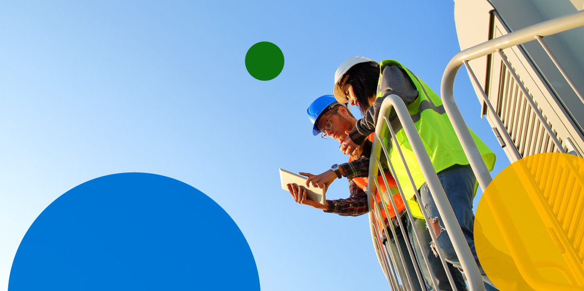 Two adults stand next to railing wearing safety vests with blue sky in background.