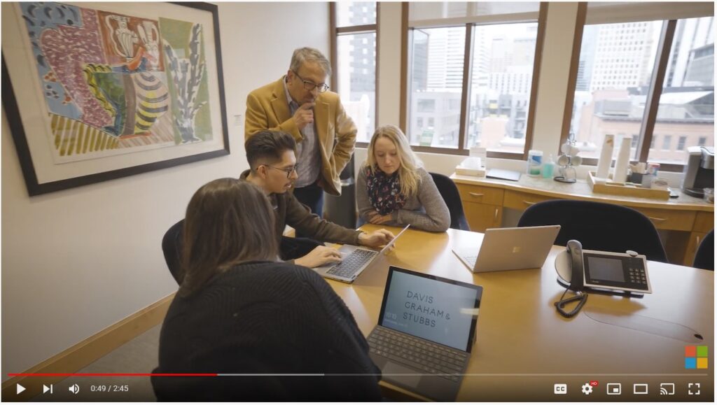 Group of professionals huddle around laptop in modern office to collaborate on project.