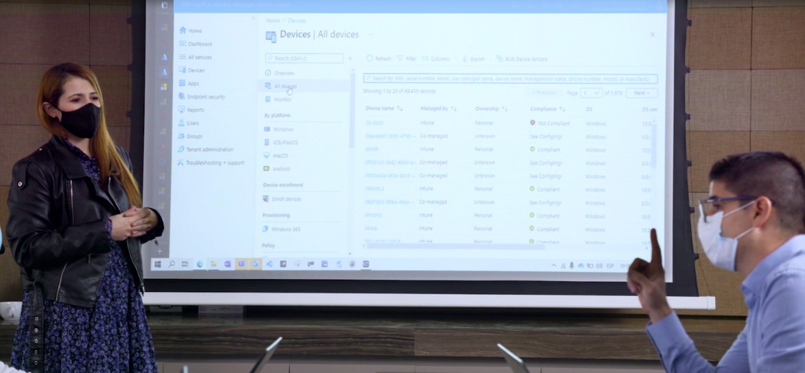 In-person meeting with a masked woman and a man discussing the information shared on screen showing the Microsoft Endpoint Manager admin center All Devices of the endpoints managed from the cloud.