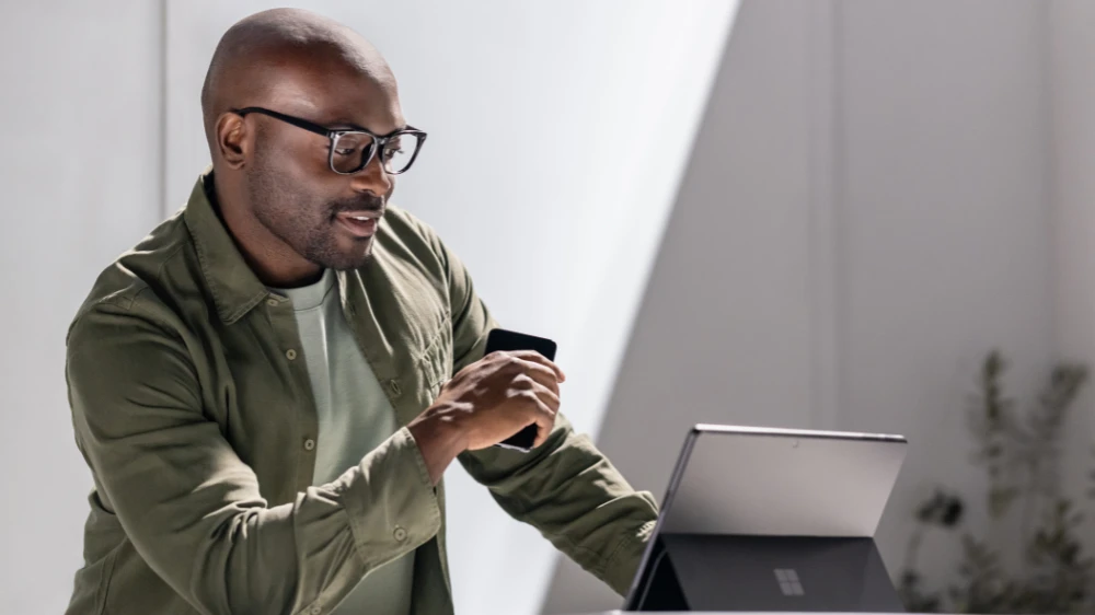 Man in focused work using a Surface tablet while holding a mobile device.