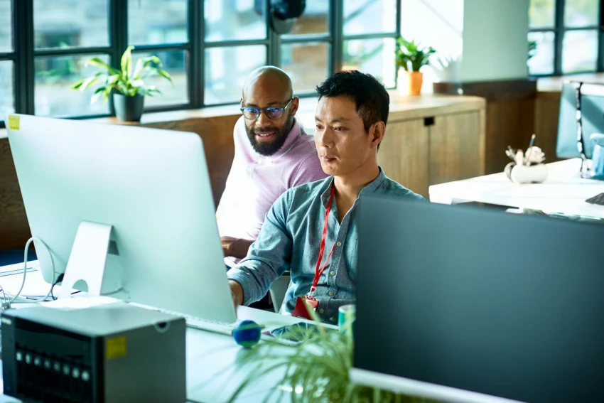Two men look at a computer screen in a sunny office.