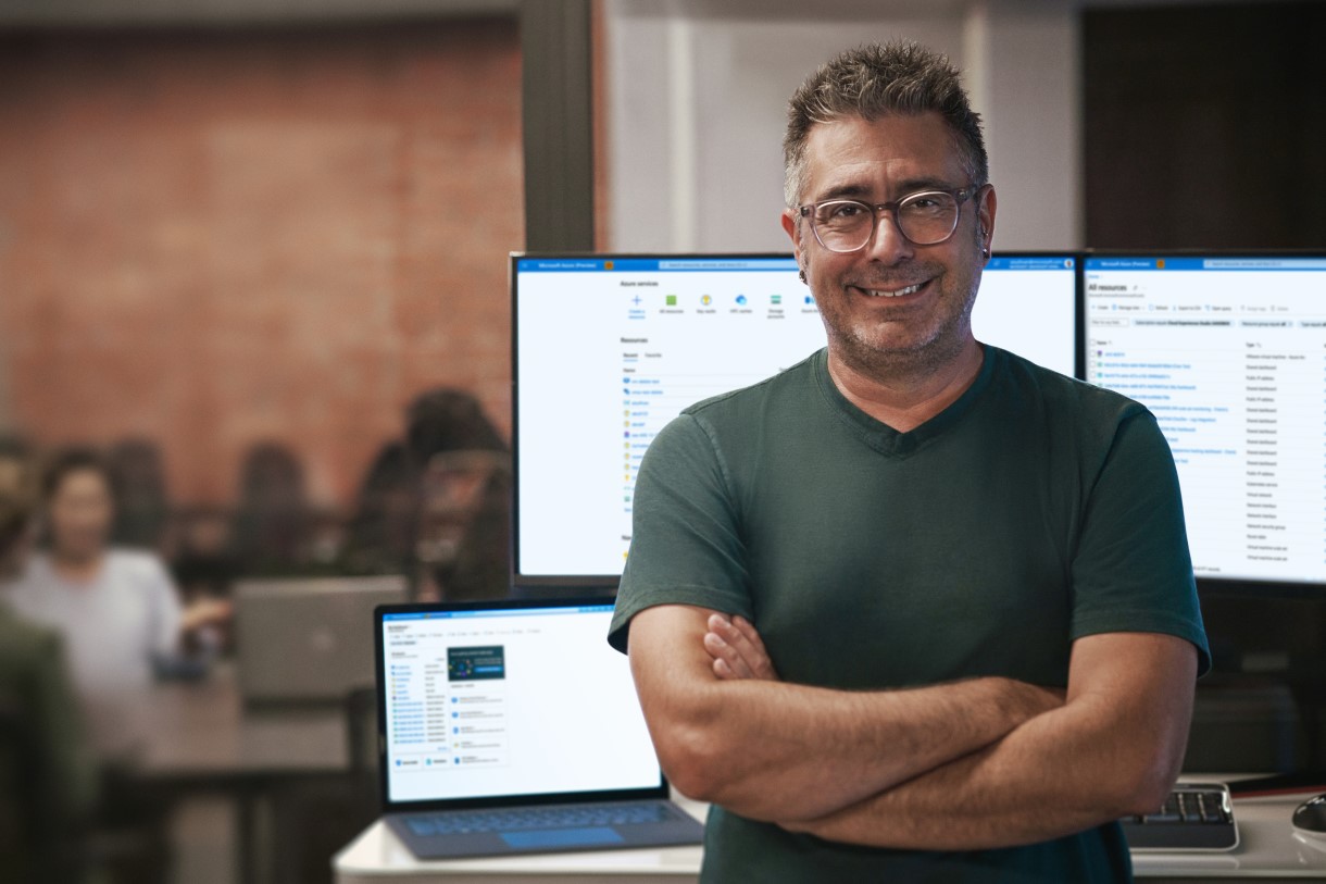 Person, in an office, standing in front of monitors.