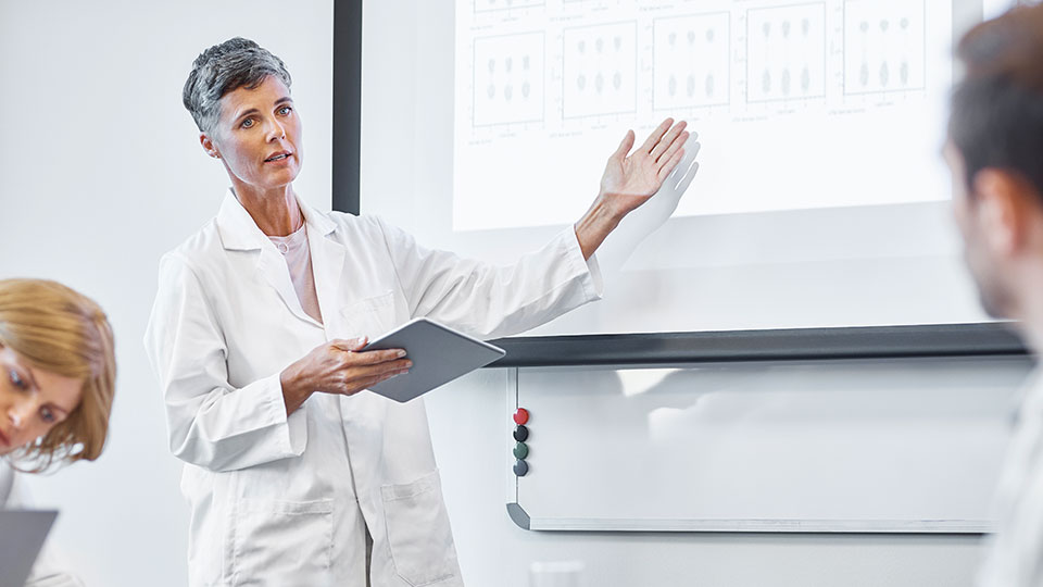 A medical professional gestures to an overhead projection