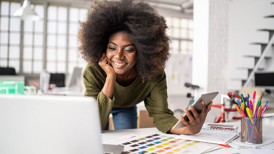 A woman holding a phone smiles at her laptop