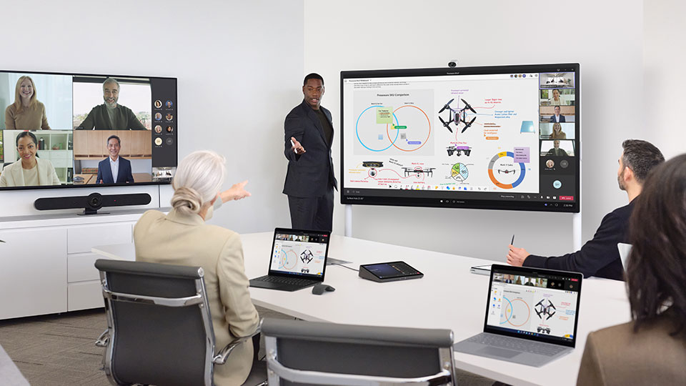 A man presents to people in a conference room and also to remote attendees