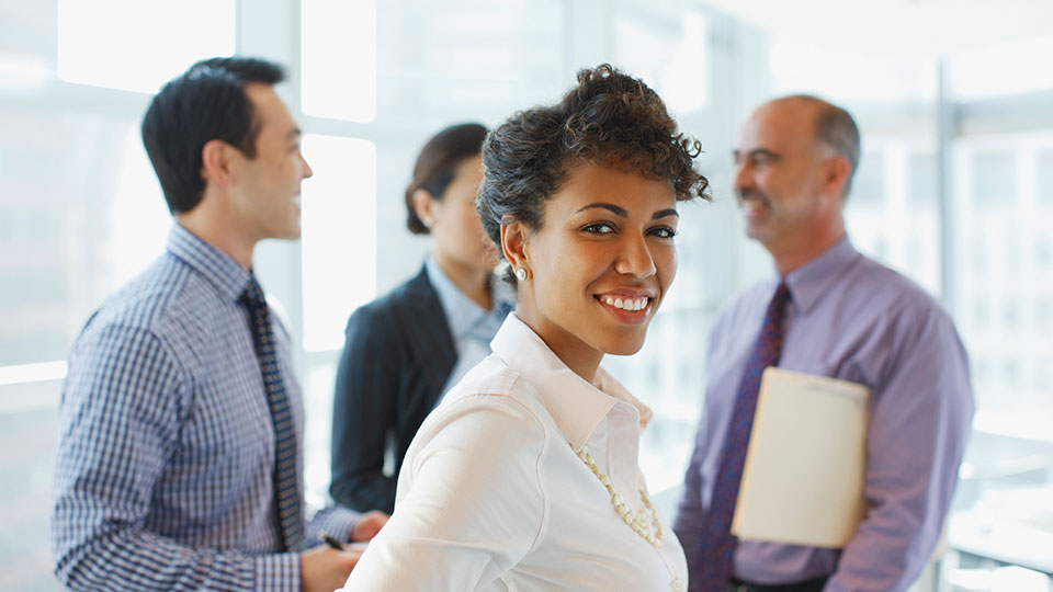 A smiling woman stands in front of coworkers having a discussion