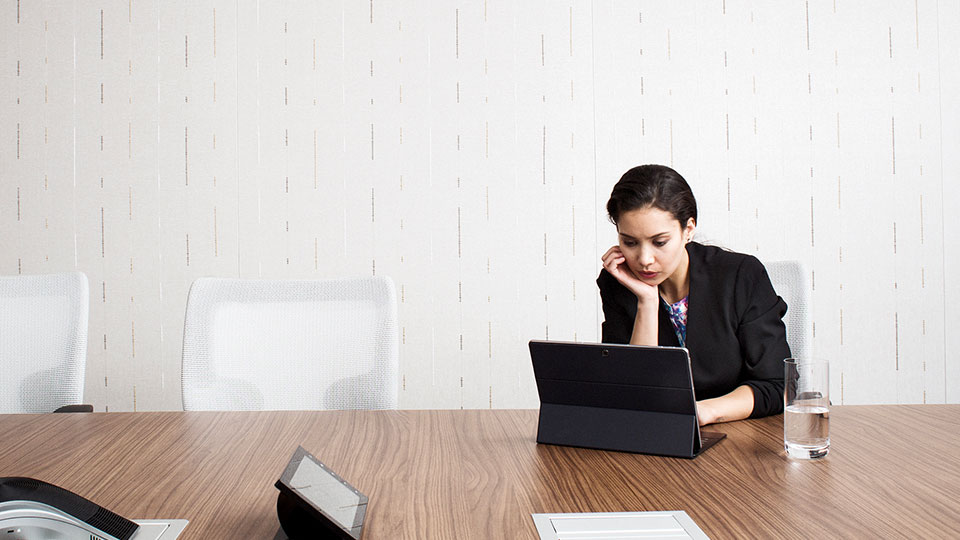 A woman sits alone at a conference table concentrating on a laptop