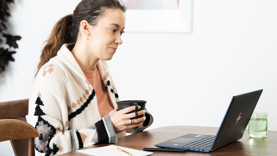 A woman holding a cup of coffee works at a laptop