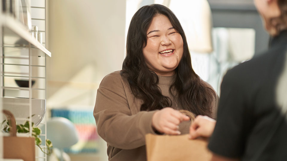 A smiling woman hands a bag to a customer