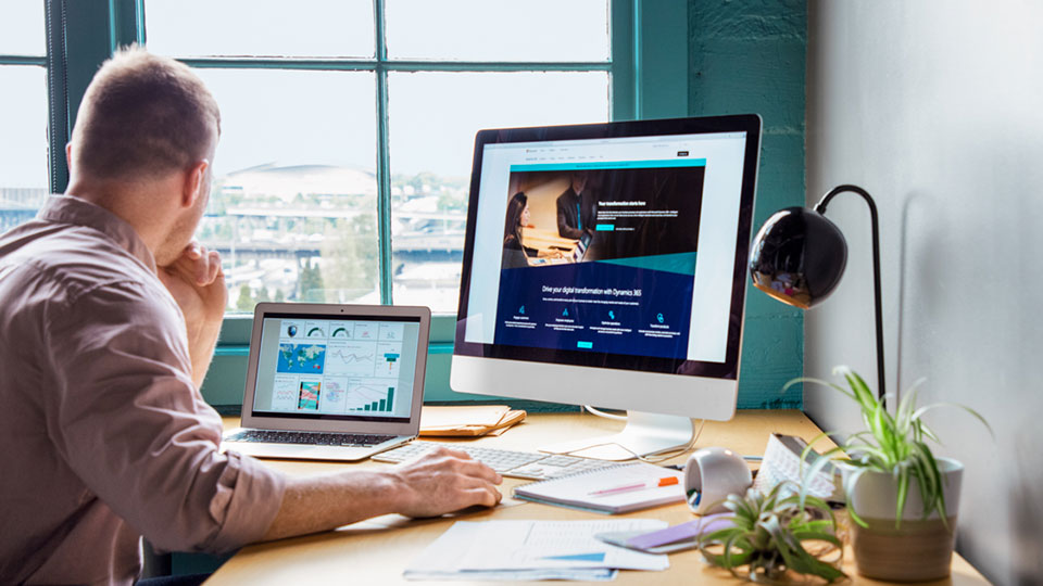 A man works at a computer workstation with a laptop and external monitor