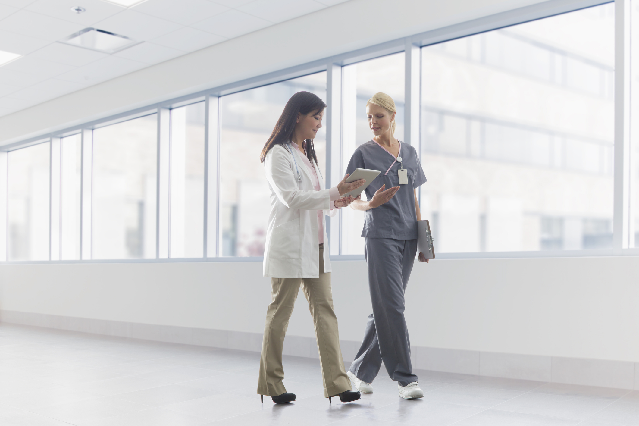 Two doctors walking down a hallway in a hospital looking at a tablet device.