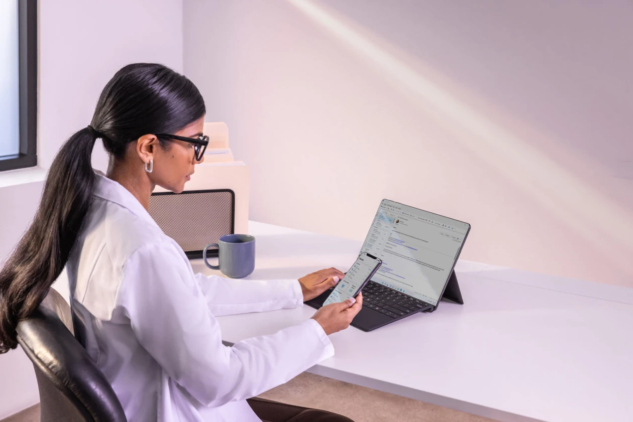 Woman sitting at desk with laptop open and cell phone in hand.