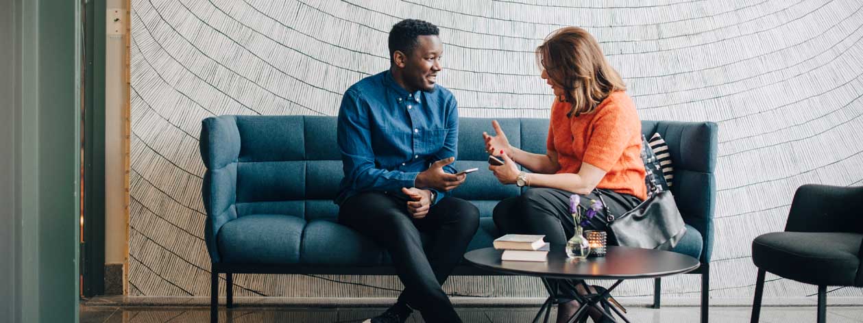Two business professionals sitting on a couch, having a conversation with their mobile devices