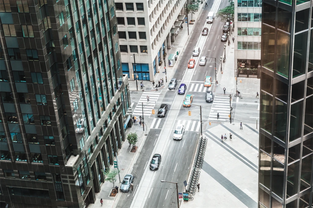 Vue de la rue du centre-ville depuis un angle élevé à l'intérieur d'un immeuble de bureaux. Les voitures traversent l'intersection dans une rue à sens unique. Quelques piétons sont visibles sur les trottoirs et aux passages pour piétons.