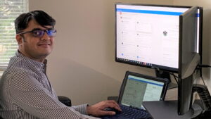 Nirav Khandhedia smiles while working at a desk in a home office.