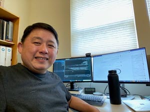 Tang sits in front of a home office set-up ad smiles at the camera.