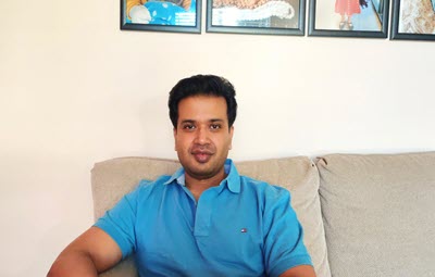 Venugopal sits on a couch in front of three paintings and smiles at the camera.