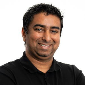 Shah poses smiling in front of a white background, wearing a black button up shirt.
