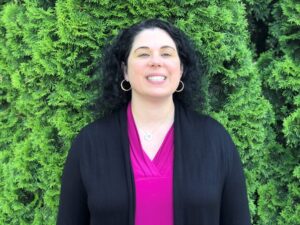 West smiles as she stands outside in front of some plants.