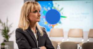 D’Hers speaks on stage with her arms folded.