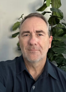LaRue poses for a portrait photo in front of a wall and plant.