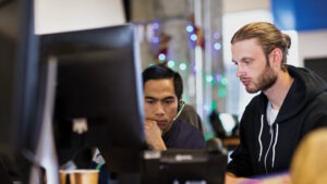 IT Professionals are sitting at a desk looking at a computer monitor.