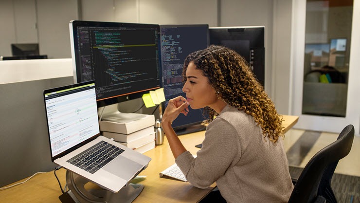 Developer working at enterprise office workspace. She has customized her workspace with a multi-monitor set up.