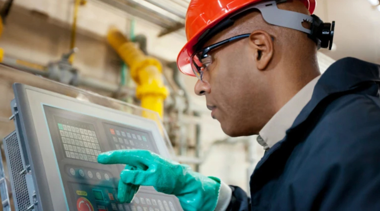 工場で操作盤をチェックする赤いヘルメットの男性