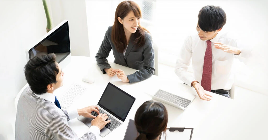 会議室で PC を使いながら話し合う男女