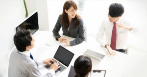 会議室で PC を使いながら話し合う男女