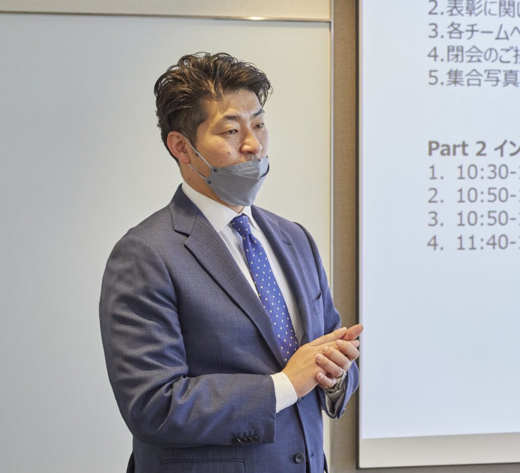 会議室で全体に向けて説明をする男性